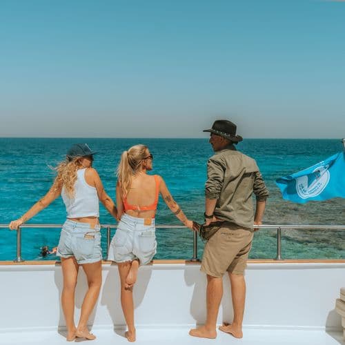 Three people standing on a boat deck looking out at the turquoise ocean.