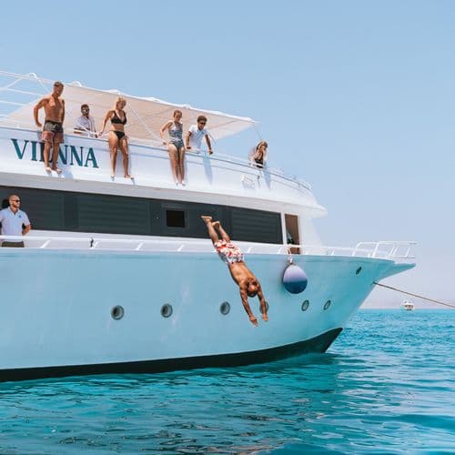 People on the top deck of a boat, one person diving into the ocean.
